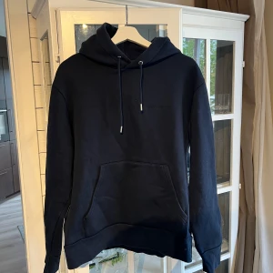 Hoodie från J.Lindeberg - Navy hoodie (chip lux sweat) från J.Lindeberg med broderad logga på bröstet. Klassisk modell med huva, dragsko och stor magficka. Mjuk insida och ribbade muddar. Perfekt för chill eller när du vill ha en clean look.