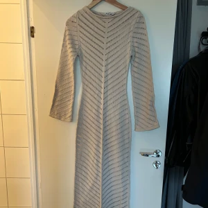 Virkad strand klänning  - Supersnygg beige långklänning från NA-KD i stickat material. Klänningen har lång ärm och ett coolt hålmönster i diagonala ränder som ger en unik look. Perfekt för dig som vill ha något bekvämt men ändå trendigt.