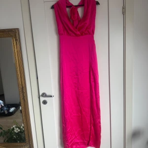 Rosa långklänning från Josefine HJ - Säljer en rosa långklänning från Josefine HJ. Klänningen har djup v-ringning, knytning i nacken och är ärmlös. Materialet är glansigt och känns lyxigt, perfekt för att sticka ut. Snygg passform och öppen rygg för en extra cool vibe.