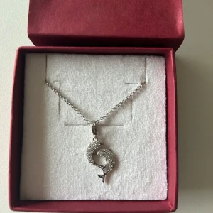 Silverhalsband med delefinhänge  - Elegant silverhalsband med ett detaljerat delefinhänge.Hänget är dekorerat med små glittrande stenar.