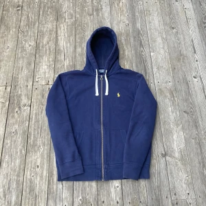 Blå hoodie från Polo Ralph Lauren - Marinblå Ralph Lauren hoodie i storlek M.              Tröjan är i mycket fint skick och har inga defekter.  Tröjan passar ungefär 173-178cm.  Hör av er om frågor!