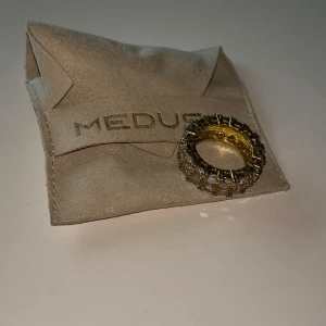 Guldfärgad ring med stenar från Medusa - Elegant guldfärgad ring från Medusa, dekorerad med glittrande stenar runt om. Perfekt för att ge en lyxig touch till din outfit.