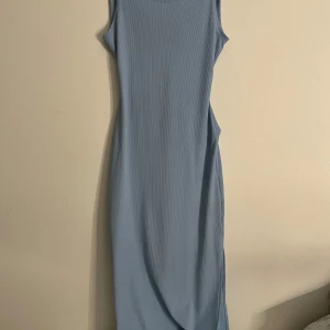 Ljusblå ribbad klänning - Snygg ljusblå ribbad klänning med ärmlös design och en stilren slits. Klänningen är i storlek S och har en öppen rygg med knytning som ger en unik touch. Perfekt för varma dagar!