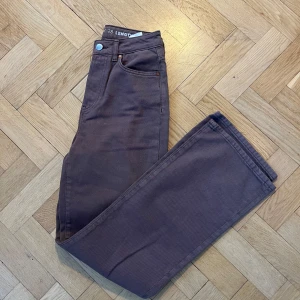 Bruna jeansbyxor från Never Denim - Snygga bruna jeansbyxor från Never Denim med en regular fit och wide stil. Byxorna har en klassisk femficksdesign och knappgylf. Perfekta för en avslappnad look.