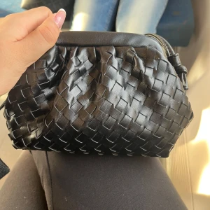 Svart flätad dumpling bag - Snygg svart dumplingbag med flätat mönster. Väskan är köpt på en marknad i Thailand så vet inte vilket märke det är. Den är använd 1-2 gånger, inga skador eller defekter är synliga på väskan! 🩷