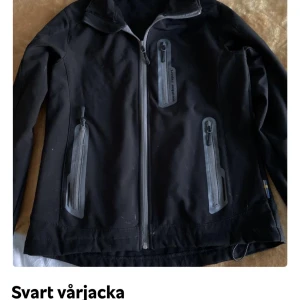 Svart vårjacka med dragkedjor - Snygg svart vårjacka med flera praktiska dragkedjor framtill. Jackan har en normal passform och är perfekt för säsongen. Den har långa ärmar och en stilren design. Ena kardborre handled lite sliten men inget som stör.
