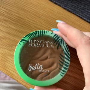 Butter Bronzer från Physicians Formula - Säljer en Butter Bronzer från Physicians Formula. Den har en krämig konsistens och kommer i en mintgrön förpackning med tropiskt mönster. Perfekt för att ge ansiktet en solkysst look.
