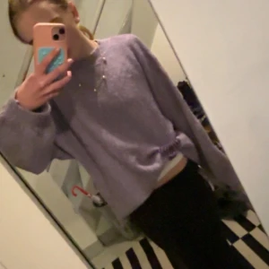 Lila stickad tröja - Mysig lila stickad tröja med långa ärmar och en avslappnad passform. Perfekt för kyligare dagar när du vill hålla dig varm och bekväm. Tröjan har en enkel design som gör den lätt att matcha med olika outfits. 