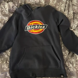 Mörkblå hoodie från Dickies - Säljer en mörkblå hoodie från Dickies med det klassiska logotyptrycket på framsidan. Tröjan har en stor ficka framtill och justerbar huva med dragsko. Perfekt för en avslappnad stil💕