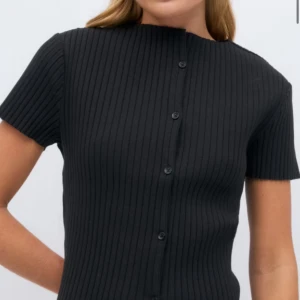 Svart ribbad kortärmad topp med knappar - Snygg svart ribbad topp med korta ärmar och knappar framtill. Perfekt för en stilren look. Har precis fått hem toppen men beställde två storlekar! Helt ny med prislapp kvar! 💗💗 slutsåld på hemsidan!