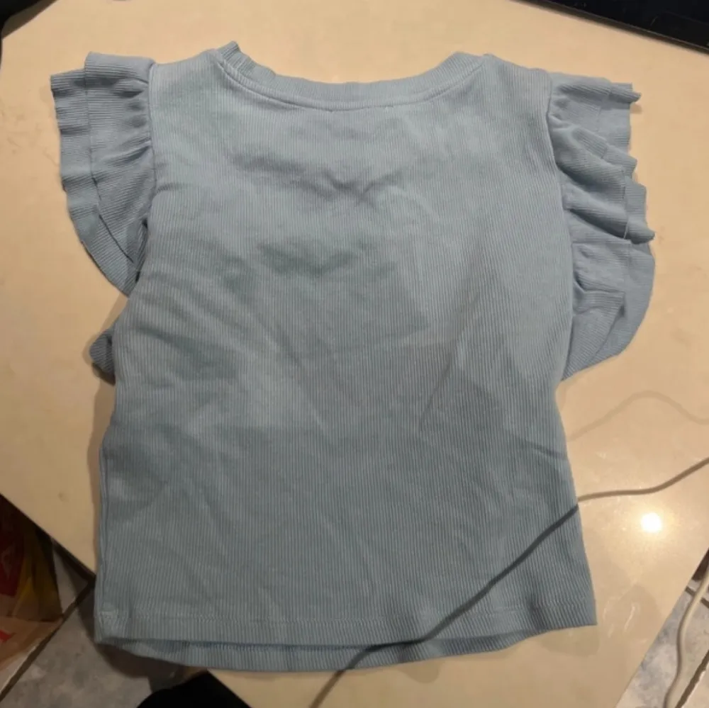 Säljer en söt ljusblå ribbad topp från Zara med volangdetaljer på ärmarna. Toppen har en rund halsringning och korta ärmar. . Yläosat.