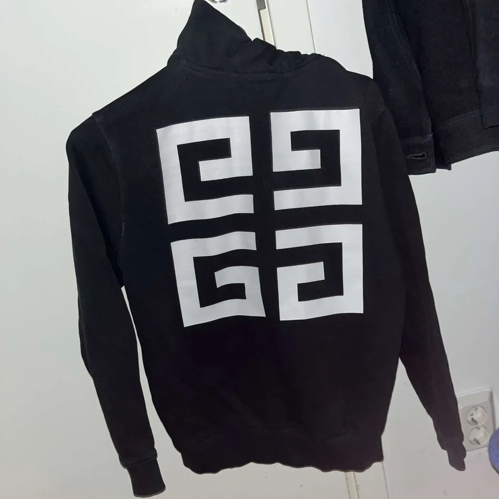 Säljer en stilren svart hoodie från Givenchy med vit logotyp på framsidan och ett grafiskt mönster på baksidan. Tröjan har dragkedja och långa ärmar, perfekt för en casual look. 100% äkta direkt köpt från NK barnavdelning Nypris 2500kr. Neuletakit & Villapaidat.