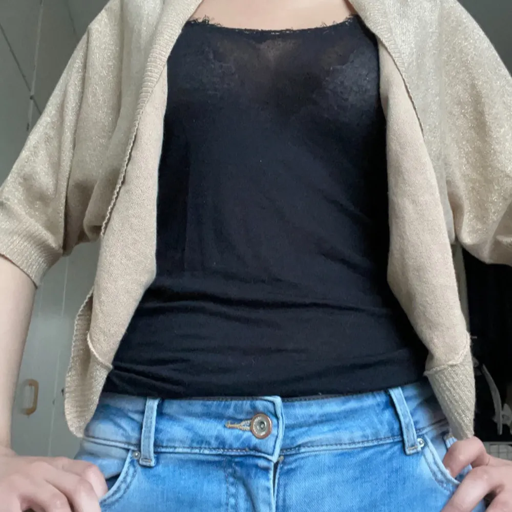 Snygg guldglittrig bolerotopp med korta ärmar. Perfekt för att lägga till lite glamour till din outfit. Passar bra över en enkel topp för en festlig look.. Neuletakit & Villapaidat.