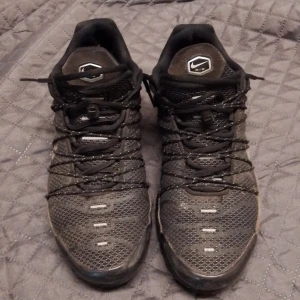 Svarta Nike sneakers - Säljer ett par svarta Nike sneakers med snörning och meshdetaljer. Skorna har en robust sula och är perfekta för en sportig look. De har en diskret Nike-logga på sidan och Tn-märke på hälen.