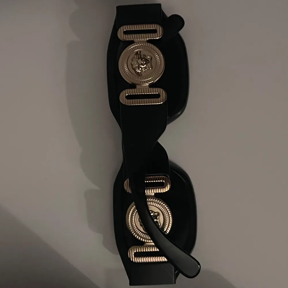 Svarta solglasögon från Versace. De har en gulddetalj med Versace-logotypen på sidorna. Knappt använda, bara några enstaka gånger så de är i ny skick.. Asusteet.