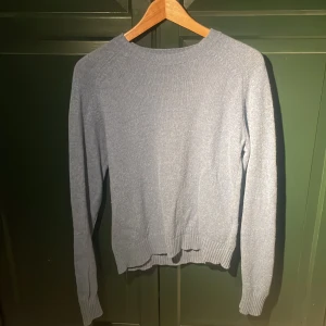 Blå stickad tröja från Uniqlo - Säljer en stilren blå stickad tröja från Uniqlo. Tröjan har en klassisk rund hals och långa ärmar med ribbade muddar. Perfekt för kyligare dagar.