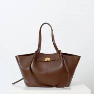 Brun trendig axelväska från Gina  - Säljer min bruna axelväska med en gulddetalj på framsidan från gina tricot, då den inte kommer till användning längre. Väskan är rymlig och har band som går att justera. Den är i nyskick då jag endast använt den 2 gånger 