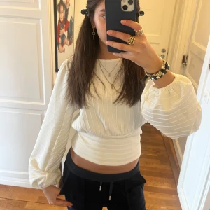 Vit ribbad topp med puffärmar - Säljer en stilren vit ribbad topp med långa puffärmar. Toppen har en tight passform och är perfekt för en trendig look. Den har en rund hals och är tillverkad i ett mjukt material.