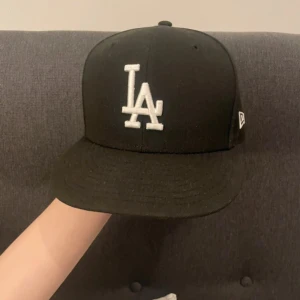 Svart keps från New Era - Snygg svart keps från New Era med vit broderad logga framtill. Kepsen är tillverkad i 100% polyester och har en klassisk design med platt skärm. Perfekt för en stilren look.