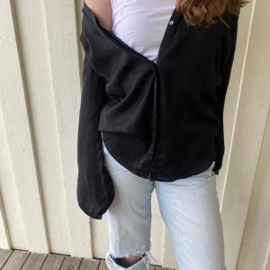 Svart skjorta med knappar - Snygg svart skjorta med knappar framtill. Tillverkad i polyester och viskos, vilket ger en mjuk och bekväm känsla. Perfekt för en stilren look. Ser ut som silke. Helt spot on. Jätte trendig just nu. 