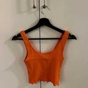 Orange ribbad linnetopp - Snygg orange ribbad linnetopp med breda axelband och croppad design. Perfekt för sommardagar och att matcha med höga jeans eller kjol.