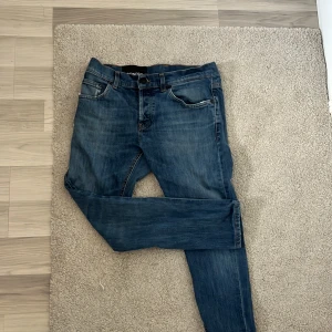 Blå jeans från Dondup - Snygga blå jeans från Dondup med klassisk femficksdesign och orange sömmar. Tillverkade i Italien, dessa jeans har en normal passform och är perfekta för en avslappnad stil. De har en dragkedja och knapp framtill. Ganska slitna men de funkar jätte bra.