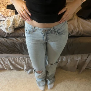 Ljusblå jeans med slitningar - Snygga ljusblå jeans med slitningar på knäna och dekorativa sömmar på bakfickorna. De har en låg midja och en straight passform. Perfekta för en avslappnad stil.