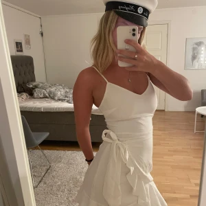 Vit omlottklänning med volang - Säljer en stilren vit omlottklänning med justeringsbara axelband och volangdetaljer. Klänningen har en knytning i midjan som ger en fin passform. Perfekt för studenten🎓👩🏼‍🎓🧑🏼‍🎓💞 