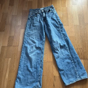 Blå jeansbyxor från H&M - Säljer ett par blå jeansbyxor från H&M med en avslappnad och bred passform. Byxorna har en klassisk femficksdesign och är perfekta för en casual look. De är tillverkade i ett slitstarkt denimtyg.