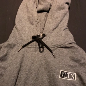 Grå hoodie från Valentino - Säljer en stilren grå hoodie från Valentino med svart VLTN-logga på bröstet.