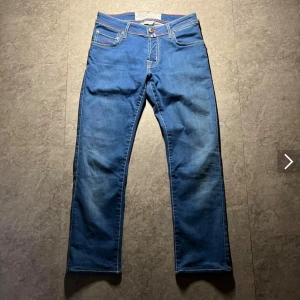 Blå jeans från Jacob Cohen - Snygga blå jeans från Jacob Cohen med klassisk femficksdesign och kontrastsömmar. Byxorna har en knappgylf och en läderpatch med logotyp baktill. Perfekta för en stilren look.