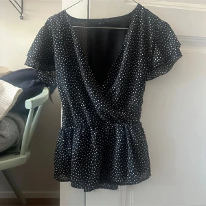 Svart prickig omlott blus - Säljer en söt svart blus med vita prickar. Blusen har en omlott-design och korta ärmar som ger en luftig känsla. Perfekt för både vardag och festliga tillfällen. Storlek 34 från Only! Aldrig använd bara testad. Perfekt nu i sommar 💞