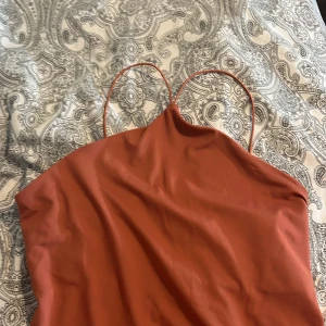 Rostfärgad axelbandslös topp - Snygg rostfärgad topp med tunna axelband. Perfekt för en somrig dag eller kväll. Topp har en enkel och stilren design som gör den lätt att matcha med olika accessoarer.