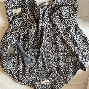 Mönstrad cardigan jacka från odd Molly  - Snygg och unik cardigan jacka från odd Molly med ett svartvitt geometriskt mönster. Jackan har en knytning i midjan och en broderad detalj på ärmen. Perfekt för att ge din outfit en cool touch!