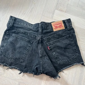 Svarta jeansshorts från Levi's - Säljer ett par coola svarta jeansshorts från Levi's med fransiga kanter och knappgylf.  midjemått 80, storlek 26, modell 501