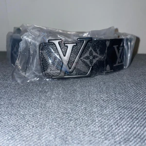 Svart bälte från Louis Vuitton - Snyggt svart bälte med det ikoniska LV-mönstret och en stilren metallspänne. Perfekt för att ge en lyxig touch till din outfit. Kommer i originalförpackning.