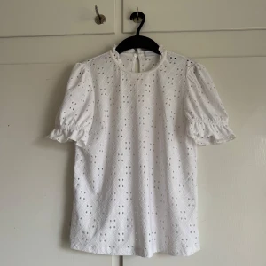 Vit blus - Säljer en söt vit blus från Vila med korta puffärmar och ett vackert broderat mönster. Perfekt för en somrig look. Blusen har en rund hals och är tillverkad i ett lätt och luftigt material. använd 1-2 gånger