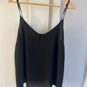 Svart linnetopp med tunna axelband - Snygg svart linnetopp med tunna axelband. Perfekt för varma dagar eller som ett lager under en kavaj. Enkel och stilren design som passar till det mesta.