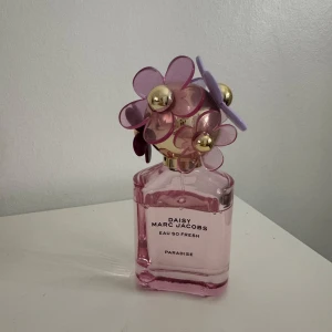 Daisy Eau So Fresh Paradise från Marc Jacobs - Säljer en Daisy Eau So Fresh Paradise parfym från Marc Jacobs. Flaskan är rosa med en unik kork dekorerad med blommor i rosa och lila samt gulddetaljer. Perfekt för den som älskar en fräsch och blommig doft. Flaskan är både elegant och lekfull, vilket gör den till en fin detalj på sminkbordet.