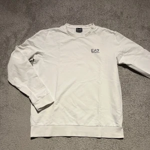 Vit långärmad tröja från Emporio Armani - Tjena tjena folket! Säljer nu en stilren vit långärmad tröja från Emporio Armani med EA7-logga på bröstet. Tröjan har en rund halsringning och är tillverkad i mjukt material för extra komfort. Pris kan även diskuteras och vidare info bara att höra av sig vid funderingar.🌟