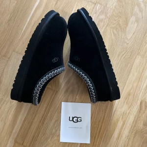Svarta mockaskor från UGG - Säljer ett par svarta mockaskor från UGG med dekorativa sömmar i kontrasterande färg. Skorna har en rund tå och en robust sula som ger bra grepp. Perfekta för kyligare dagar. Skriv gärna!