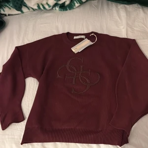 Vinröd tröja från Guess - Säljer en snygg vinröd tröja från Guess med ett dekorativt mönster på framsidan. Tröjan har långa ärmar och en rund halsringning. Perfekt för en stilren look.