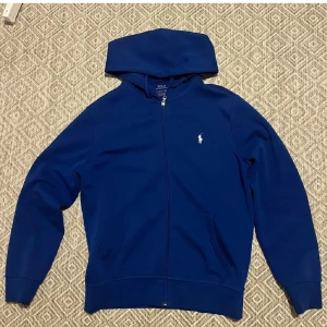 Blå hoodie från Ralph Lauren - Säljer en snygg blå hoodie från Ralph Lauren med dragkedja och det klassiska logotypen på bröstet. Storlek S köpt från Zalando och intill nyskick .