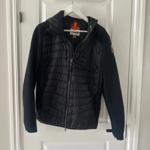 Svart jacka från Parajumpers - Säljer en svart jacka från Parajumpers med dragkedja och huva. Jackan har ett märke på ärmen och är perfekt för kyligare dagar. Den har en quiltad design på framsidan och släta ärmar.
