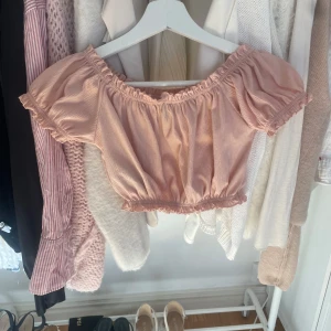 Rosa offshoulder topp från Divided - Säljer en söt rosa offshoulder topp från Divided. Toppen är croppad med volangdetaljer och har en elastisk kant vid axlar och midja för en bekväm passform. Perfekt för varma sommardagar! 🌸