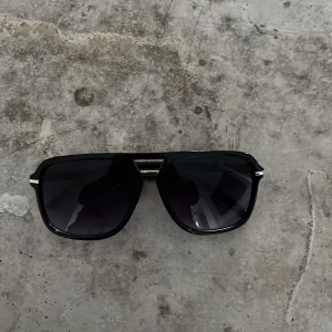 Svarta solglasögon med metallbrygga - Snygga svarta solglasögon med en cool metallbrygga och mörka linser. Perfekta för att ge en stilren look. Passar bra till både vardag och fest.