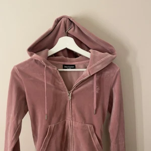 Rosa hoodie från Juicy Couture - Säljer en supermjuk rosa hoodie från Juicy Couture i velourmaterial. Den har en dragkedja framtill och en praktisk huva. Perfekt för en avslappnad stil. 💖säljer pga att den inte kommer till andvändning. Fint skick men  J*et har har tappat pytte lite av färgen men inget man tänker på. Storlek xxs. Köpt för 1200 säljer för 450kr köparen står för frakten💓 