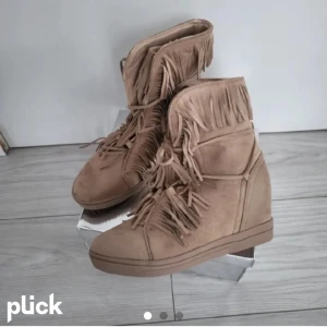 Beige boots med fransar - Snygga beige boots med fransar och snörning. Perfekta för en trendig look med en touch av boho-stil. De har en rund tå och är gjorda i mocka för en mjuk känsla.