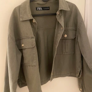 Olivgrön jacka från Zara - Säljer en olivgrön jacka från Zara med knappar framtill och två bröstfickor. Jackan har en avslappnad passform och är perfekt för vår och höst. Den har långa ärmar och en klassisk krage.