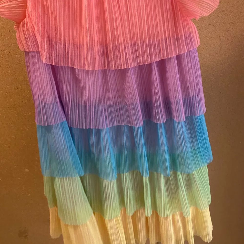 Säljer en färgglad klänning från H&M med volanger i rosa, lila, blå och gröna nyanser. Klänningen har korta ärmar och är perfekt för sommarens alla tillfällen. Den är tillverkad i ett lätt och luftigt material.. Mekot.